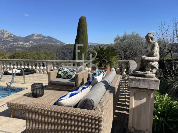 Terrasse d'une villa à Vence avec vue sur les montagnes, mobilier en osier et statue.