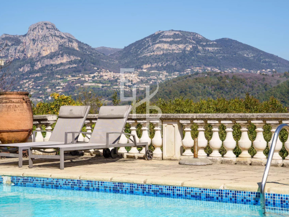 Vue sur la piscine et les montagnes depuis une villa à Vence, avec chaises longues au bord de la piscine.