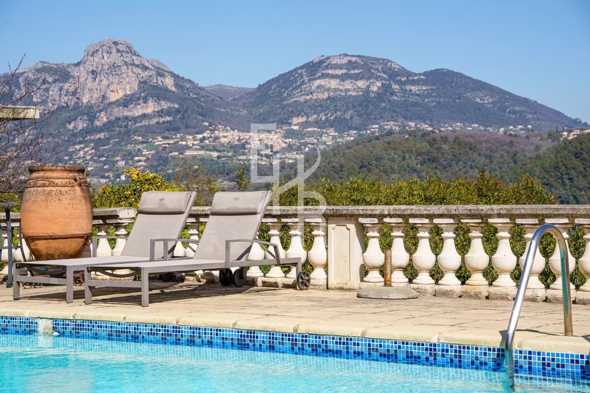 Vue sur la piscine et les montagnes depuis une villa à Vence, avec chaises longues au bord de la piscine.
