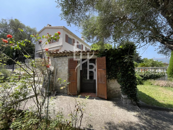Entrée d'une villa à Vence avec des portes en bois et des fleurs autour.