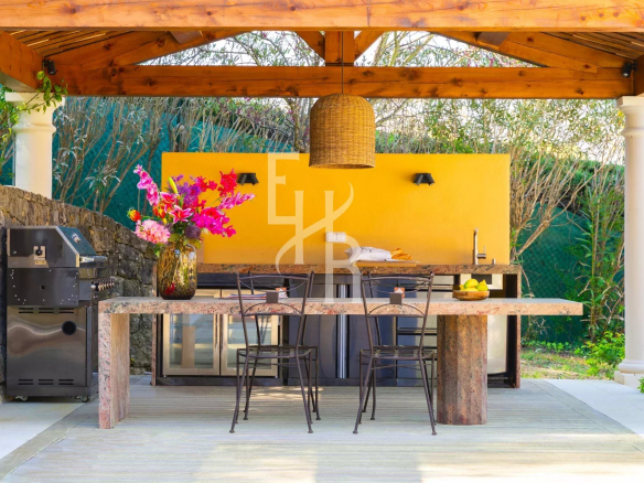 Cuisine extérieure avec table en pierre et chaises, fleurs en vase, sous un abri en bois à Mougins.