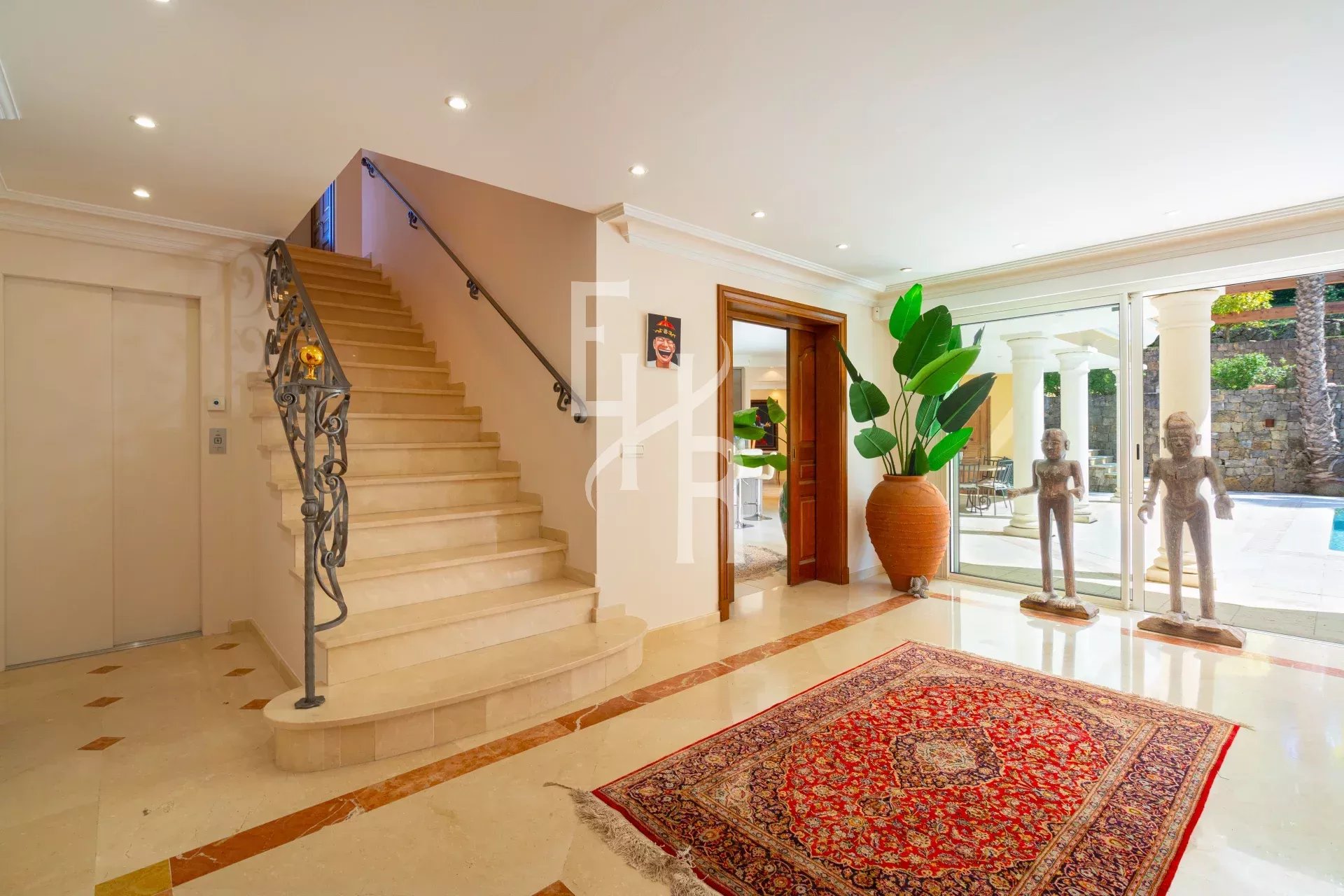 Intérieur d'une villa à Mougins avec un escalier, des sculptures et un tapis au sol.