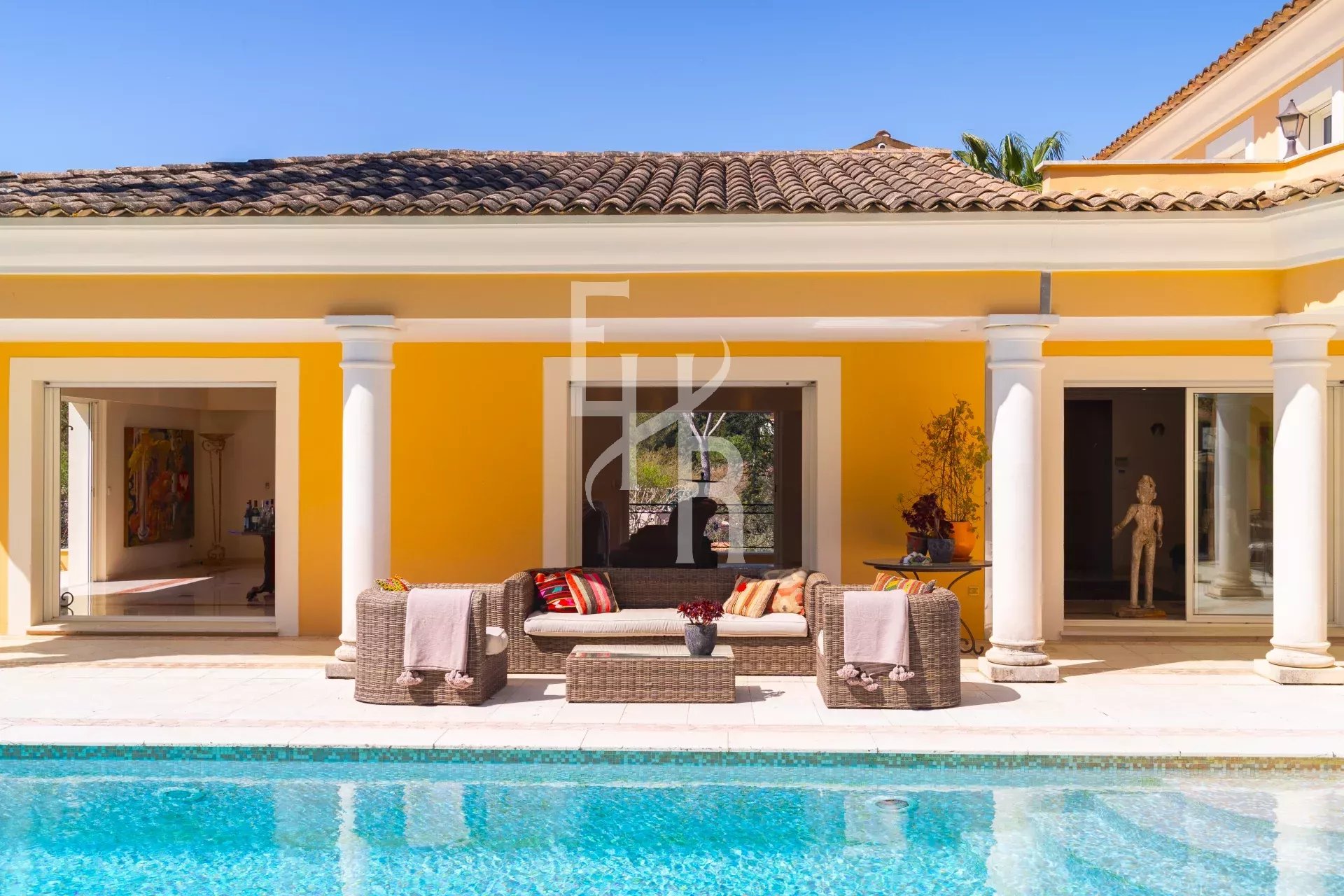 Villa avec piscine et mobilier de jardin à Mougins, murs jaunes et colonnes blanches.