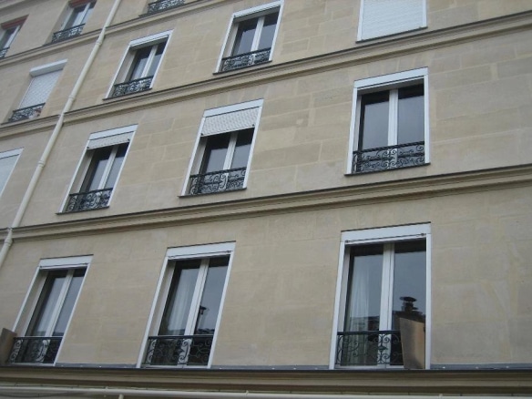 Façade d'un immeuble en pierre de taille à Paris 16ème avec fenêtres et balcons.