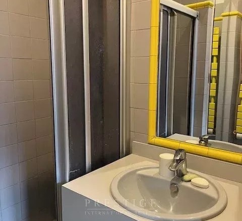Salle de bain avec douche et lavabo, décorée de carrelage gris et de détails jaunes.