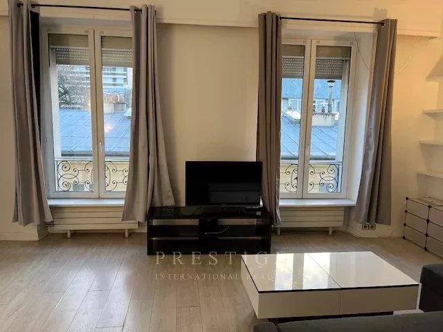 Salon d’un appartement à Paris 16ème Salon lumineux avec fenêtres et télévision, parquet clair, rideaux gris, dans un appartement à Paris 16ème.