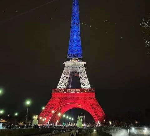 Tour Eiffel illuminée aux couleurs bleu, blanc, rouge la nuit, avec un pont au premier plan.
