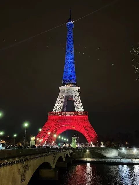 Tour Eiffel aux couleurs de la France Tour Eiffel illuminée aux couleurs bleu, blanc, rouge la nuit, avec un pont au premier plan.