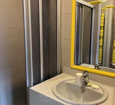 Salle de bain avec douche et lavabo, murs carrelés en gris, accessoires jaunes.