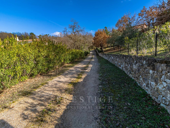Chemin menant à un terrain à bâtir à Châteauneuf-Grasse, entouré de verdure et de murs en pierre.