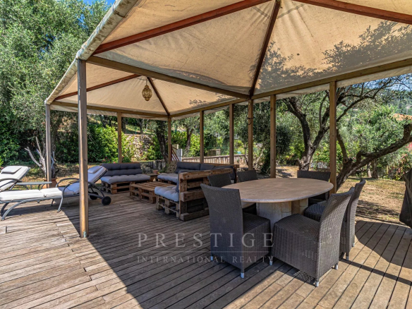 Terrasse en bois avec mobilier de jardin, entourée d'arbres et d'une végétation luxuriante.