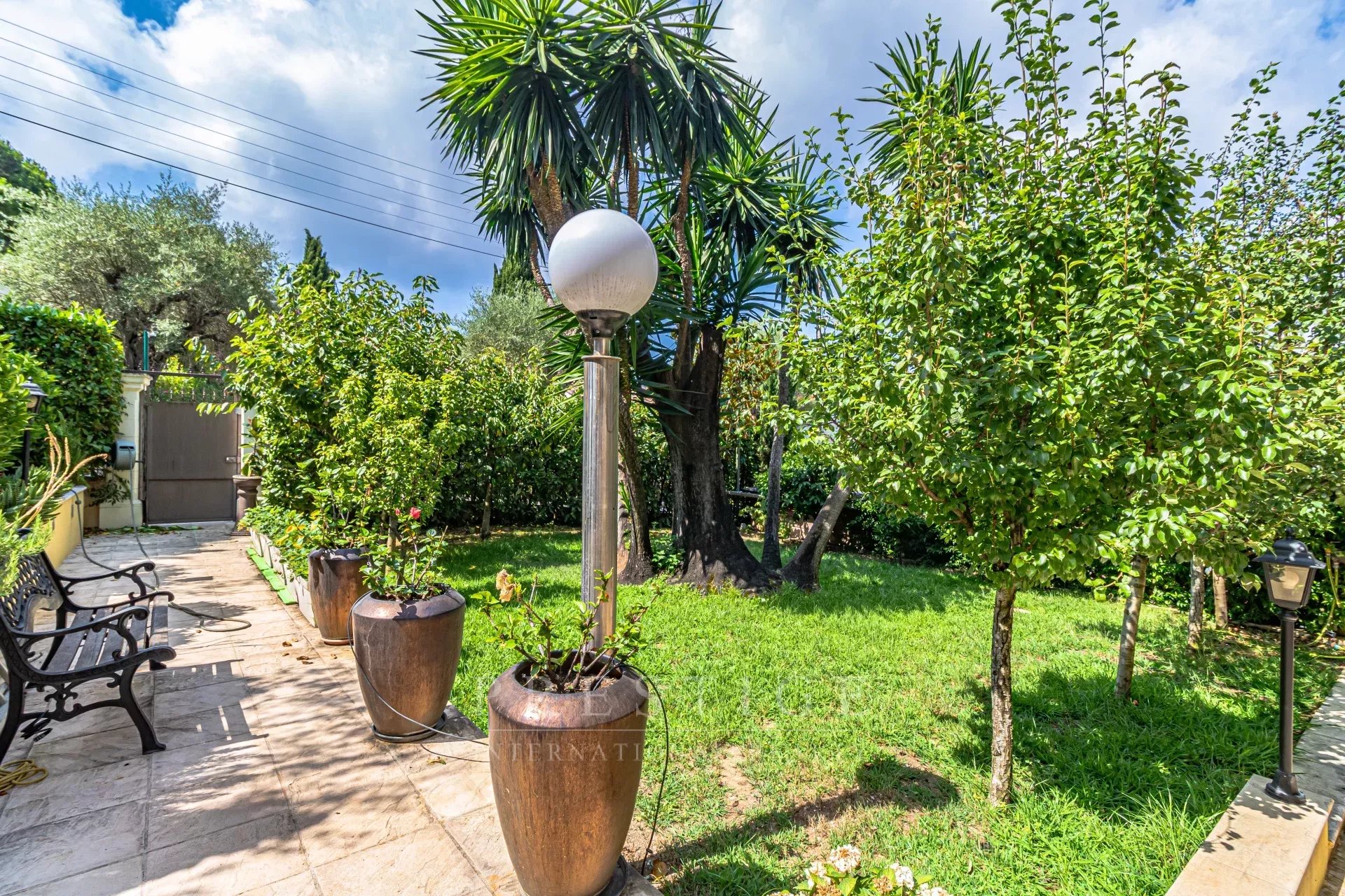 Jardin de villa au Cap d’Antibes Jardin d'une villa luxueuse au Cap d'Antibes avec des plantes et des lampadaires.
