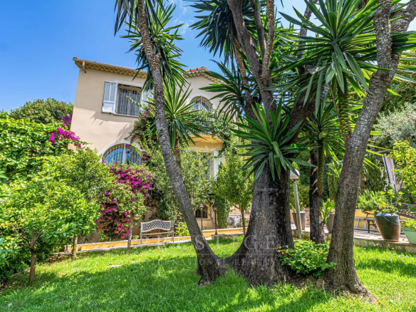 Villa luxueuse à Cap d'Antibes entourée de verdure et de palmiers.