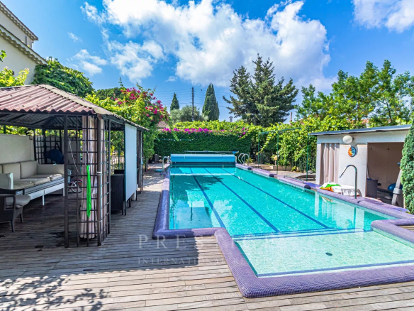 Piscine d'une villa luxueuse à Cap d'Antibes, entourée de verdure et de terrasses en bois.