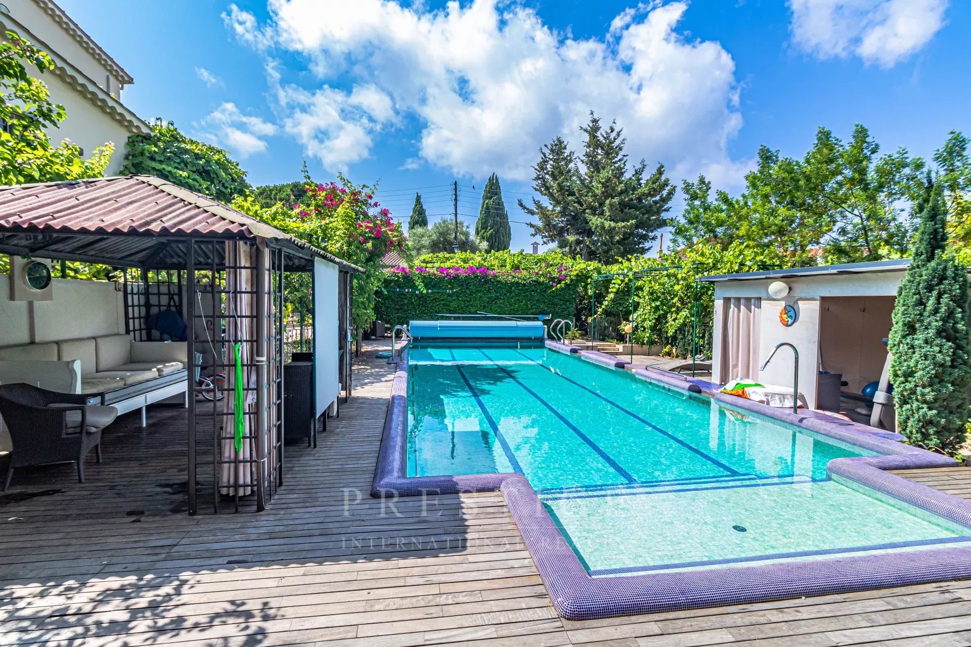 Villa avec piscine à Cap d’Antibes Piscine d'une villa luxueuse à Cap d'Antibes, entourée de verdure et de terrasses en bois.