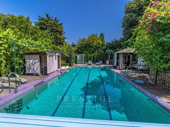 Piscine d'une villa luxueuse à Cap d'Antibes, entourée de verdure.