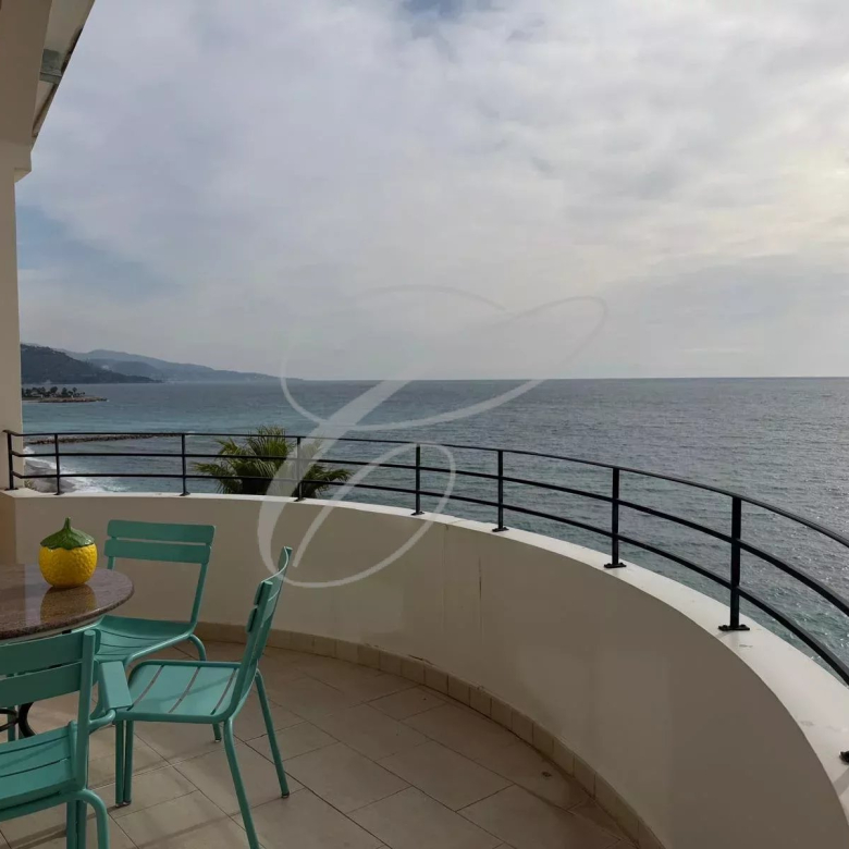 Ocean view from a curved balcony with turquoise chairs and a round table topped by a yellow decorative item, overlooking the sea.