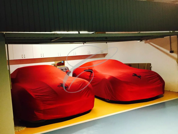 Two red Ferrari-covered sports cars parked side by side in a tidy garage with white upper cabinets above them.