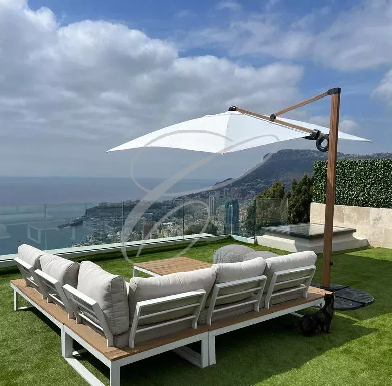 Outdoor rooftop lounge with white cushioned sectional sofa, a large white umbrella, and an ocean view.
