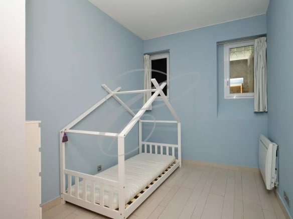 Bedroom in an apartment in Beausoleil with a white wooden bed and blue walls.