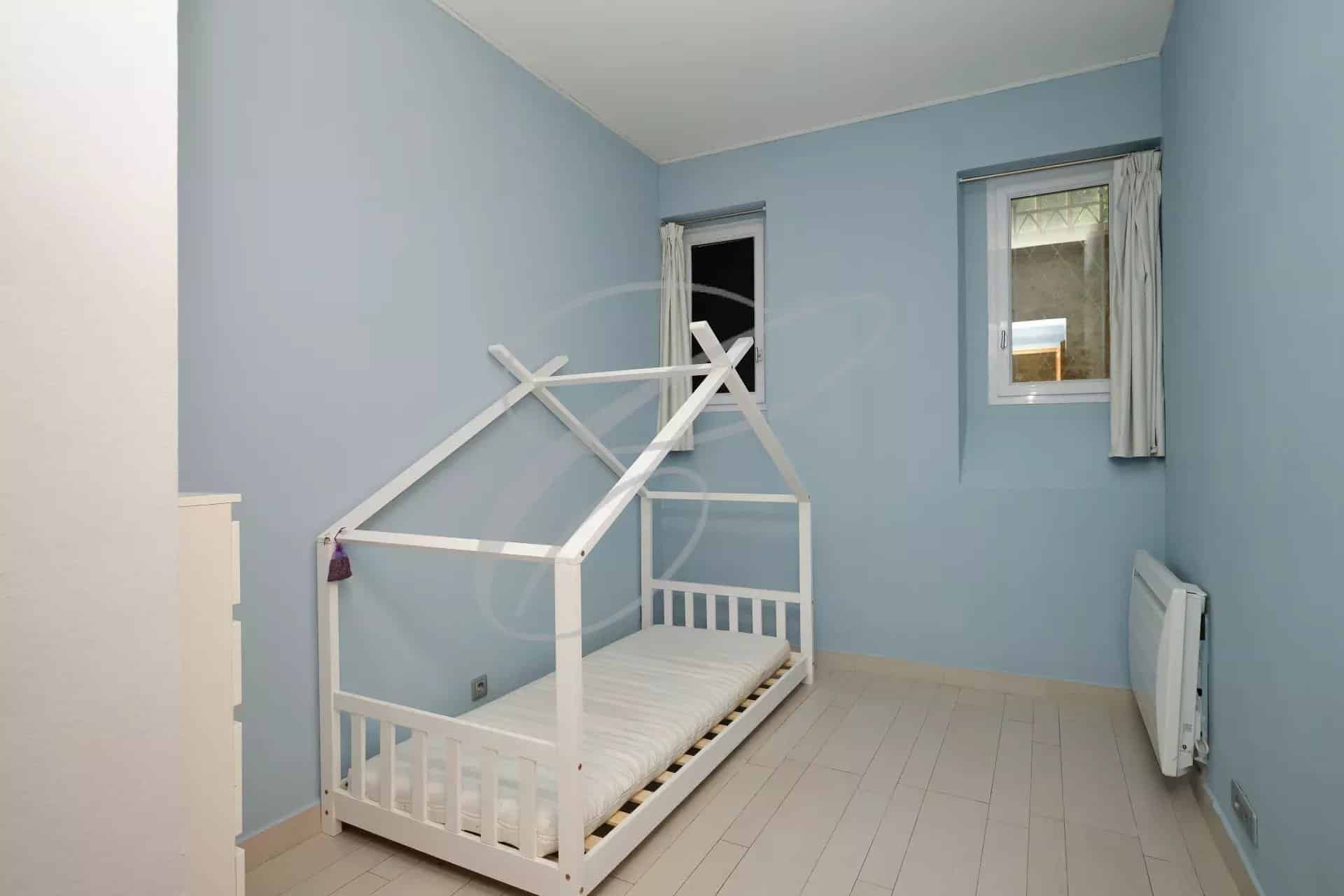 Bedroom in an apartment in Beausoleil with a white wooden bed and blue walls.