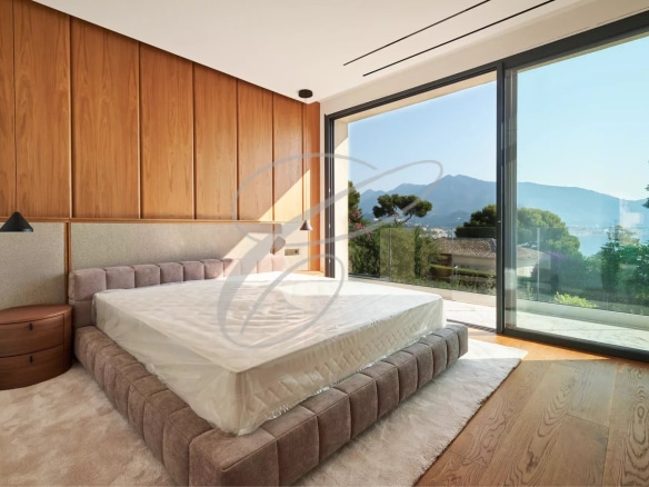 Modern room with bed and large window offering a view of the garden and the sea.