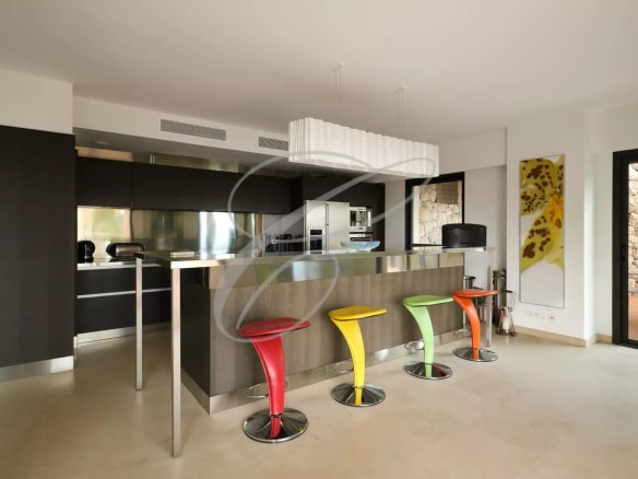 Cuisine moderne avec bar à petit déjeuner et chaises colorées dans une villa contemporaine.