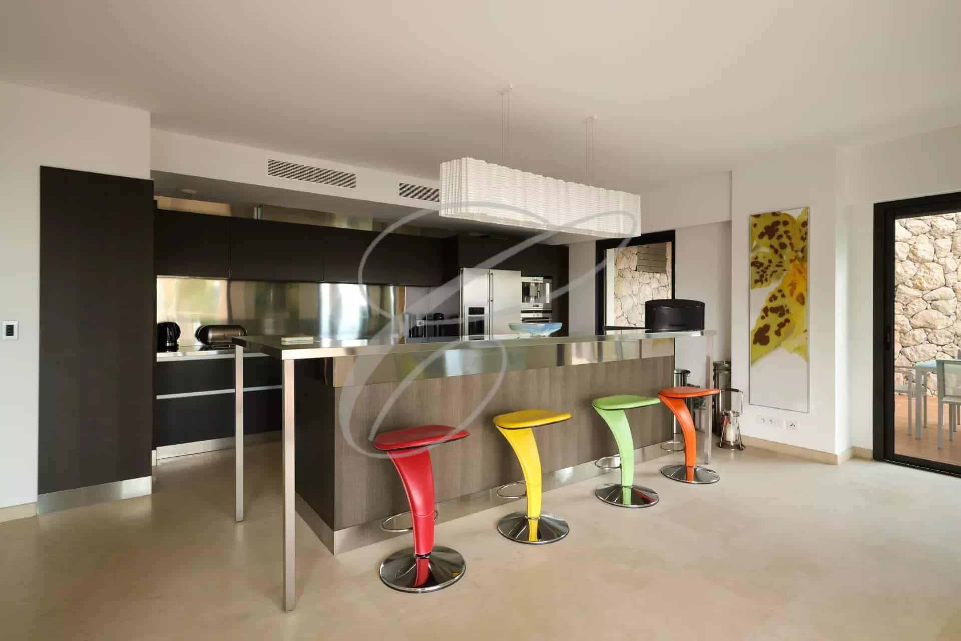 Cuisine moderne avec bar à petit déjeuner et chaises colorées dans une villa contemporaine.