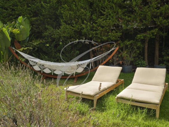 Outdoor space of an apartment with deckchairs and hammock in a green garden.