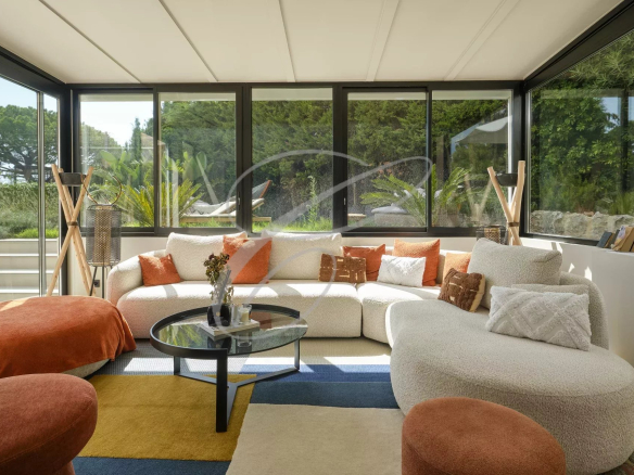 Bright living room with sofa and coffee table, windows overlooking a garden.