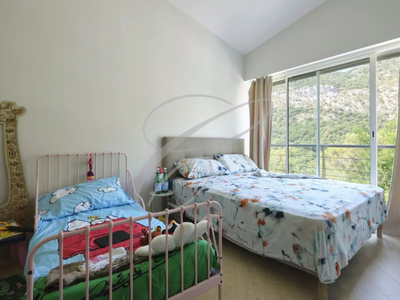 Chambre d'une villa moderne avec lit double et lit bébé, fenêtres donnant sur la nature.
