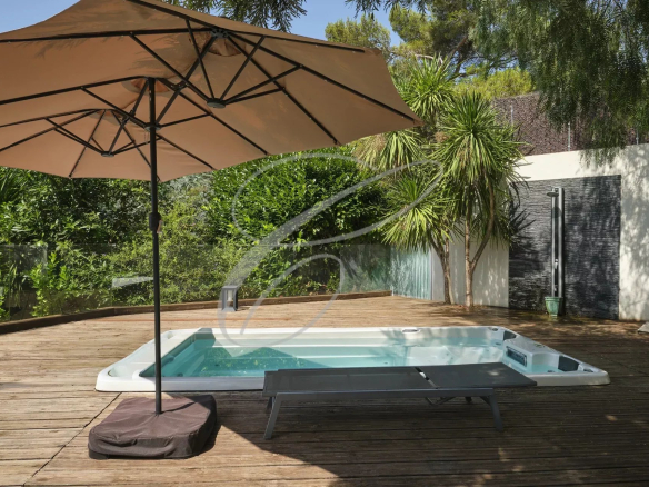 Terrasse en bois avec jacuzzi et parasol, entourée de verdure dans une villa moderne.