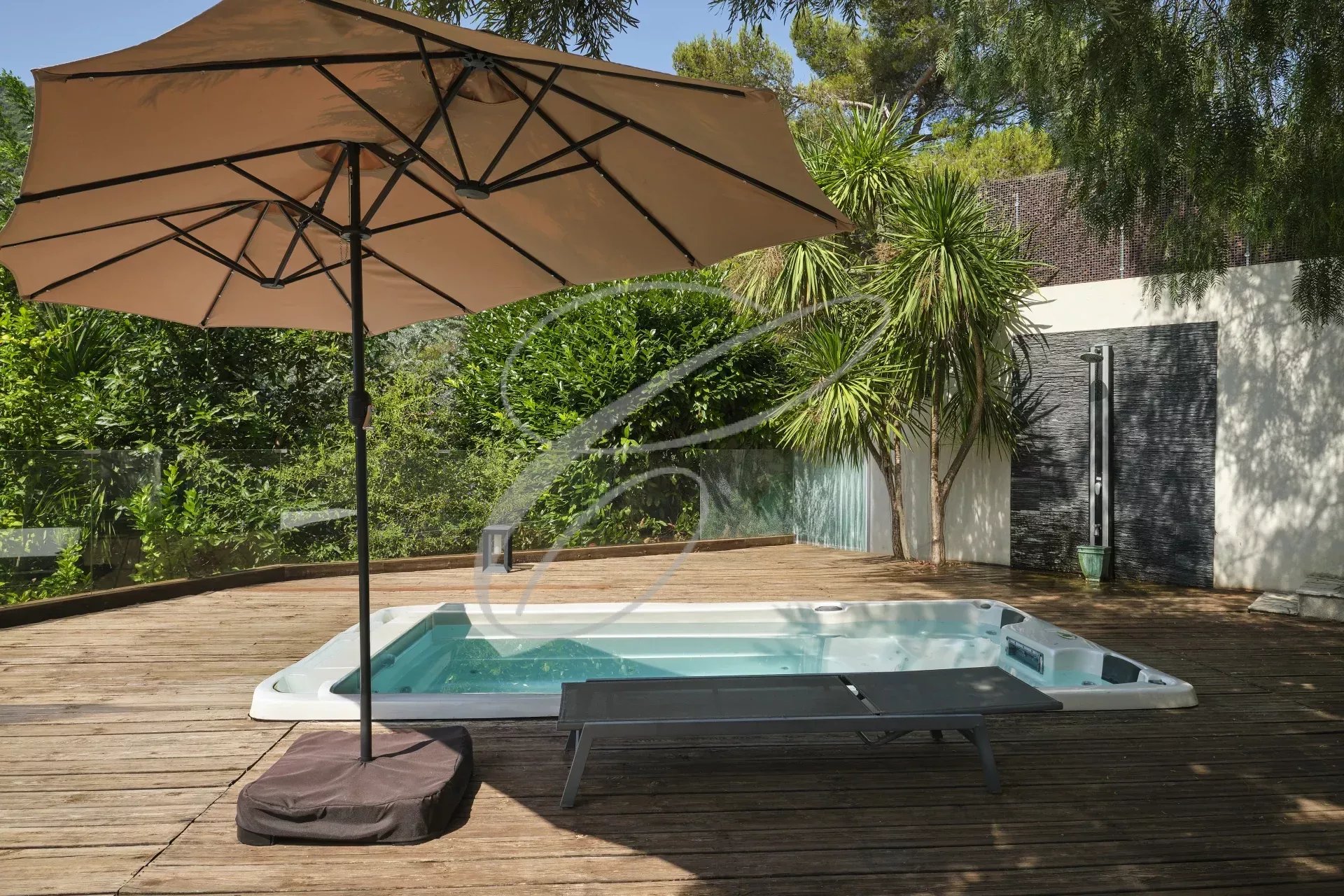 Terrasse avec jacuzzi dans une villa moderne Terrasse en bois avec jacuzzi et parasol, entourée de verdure dans une villa moderne.