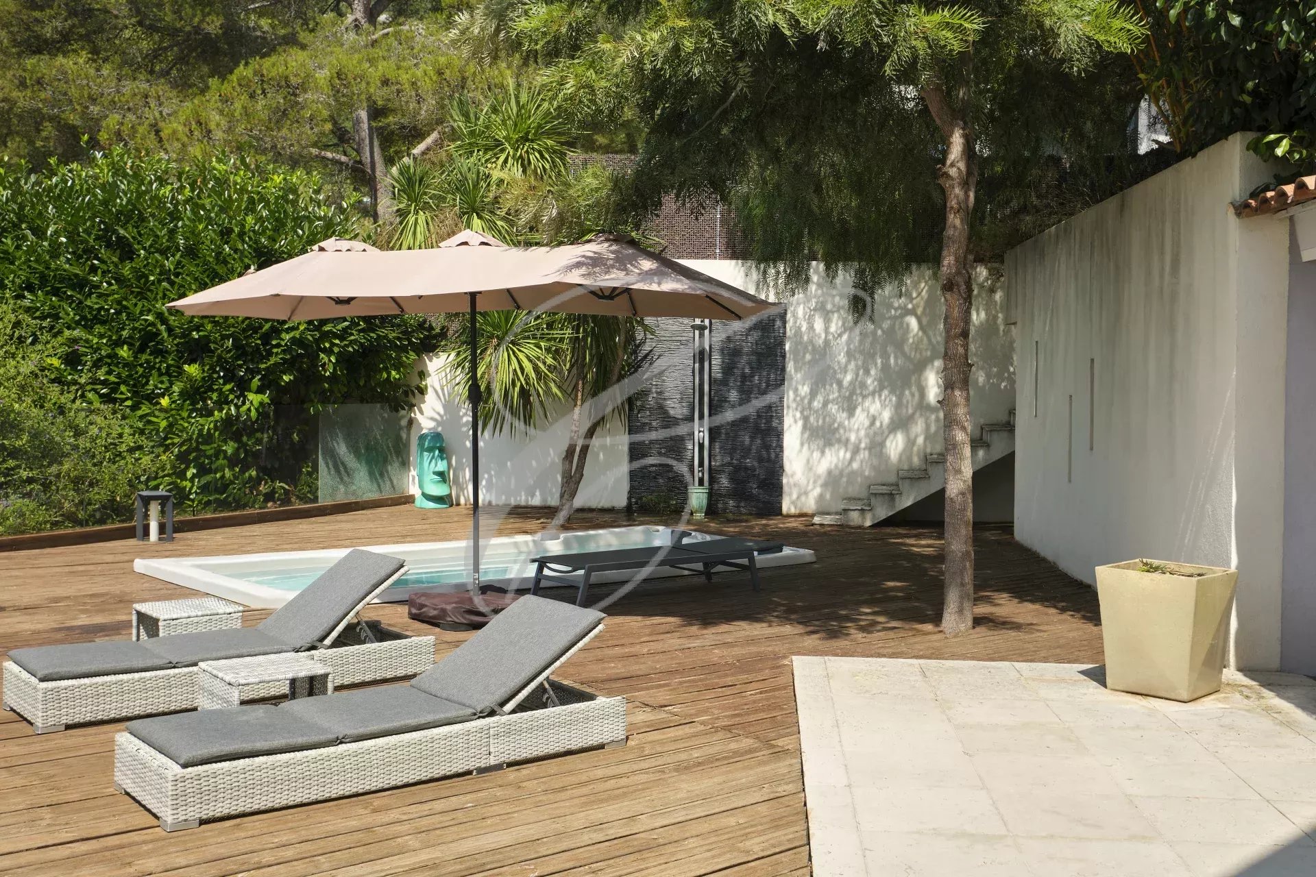 Terrasse avec jacuzzi d’une villa moderne Terrasse d'une villa moderne avec jacuzzi, chaises longues et parasol, entourée de verdure.