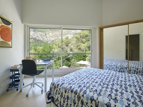 Chambre d'une villa moderne avec vue sur la nature, fenêtres larges et décoration simple.