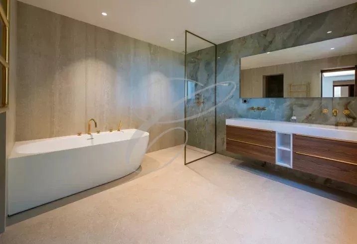 Salle de bains moderne avec baignoire et meuble double vasque, murs en pierre.