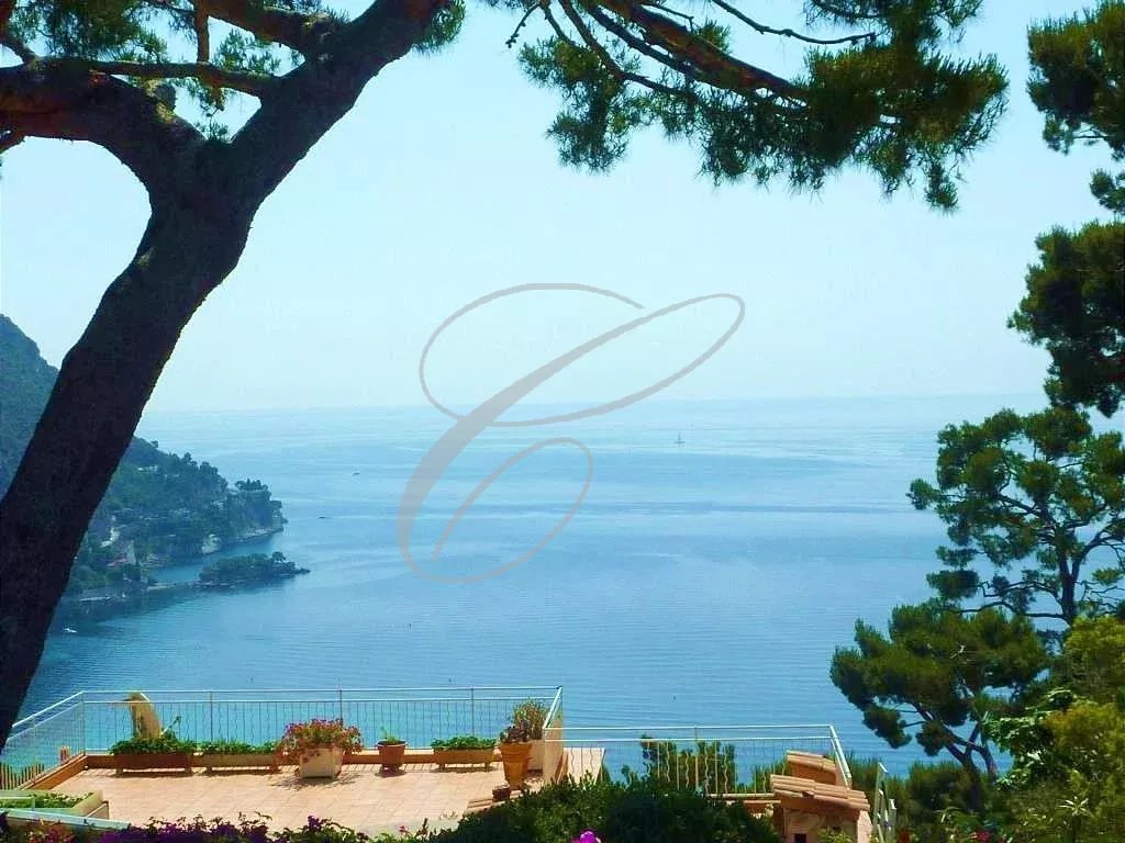 Vue panoramique sur la mer depuis une villa à Èze, avec des arbres en premier plan.