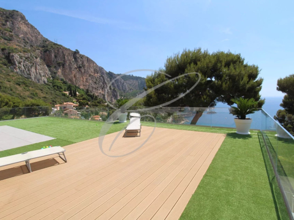 Terrasse en bois d'une villa à Èze avec vue sur la mer et les montagnes environnantes.