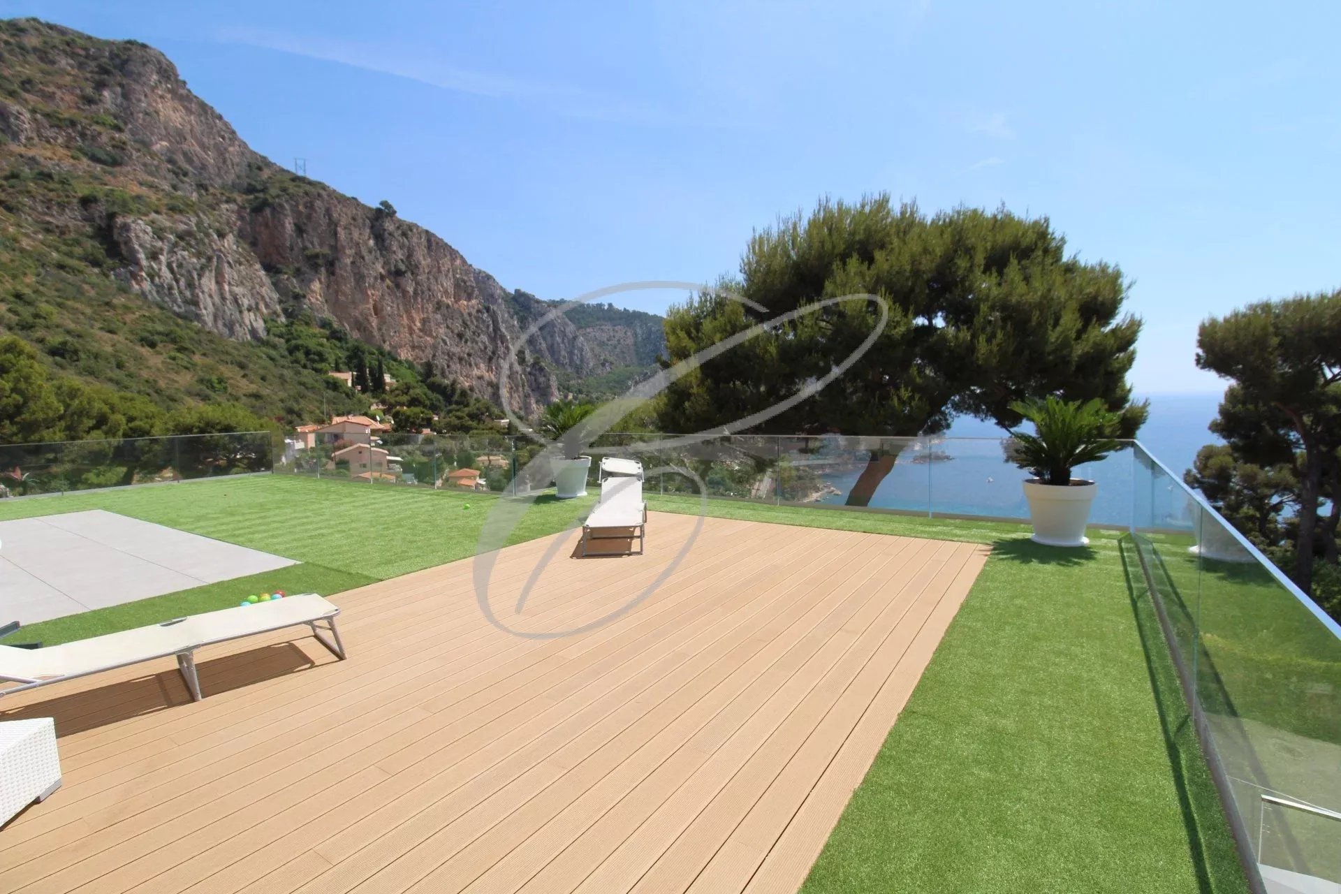 Terrasse en bois d'une villa à Èze avec vue sur la mer et les montagnes environnantes.