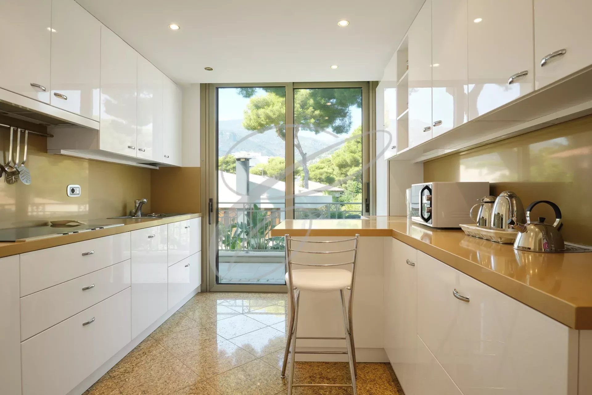 Cuisine moderne avec meubles blancs et plan de travail en bois, vue sur l'extérieur.