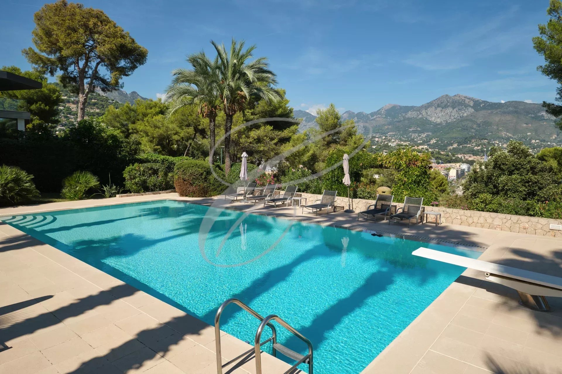 Piscine d'une résidence de luxe à Roquebrune-Cap-Martin, entourée de verdure et de montagnes.