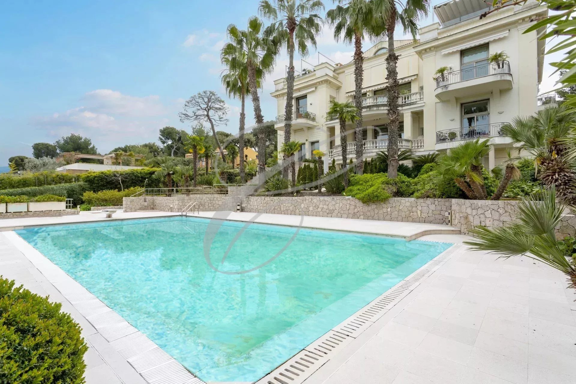 Piscine d'une résidence de luxe à Roquebrune-Cap-Martin, entourée de palmiers et de verdure.