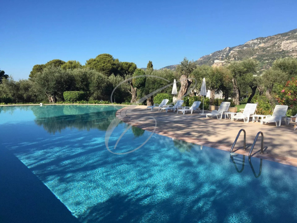 Piscine d'une résidence avec chaises longues et vue sur la nature environnante à Roquebrune-Cap-Martin.