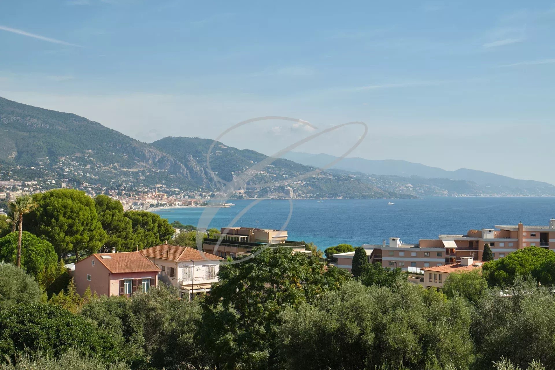 Vue panoramique sur la mer et Monaco depuis Roquebrune-Cap-Martin, avec des bâtiments et des arbres au premier plan.