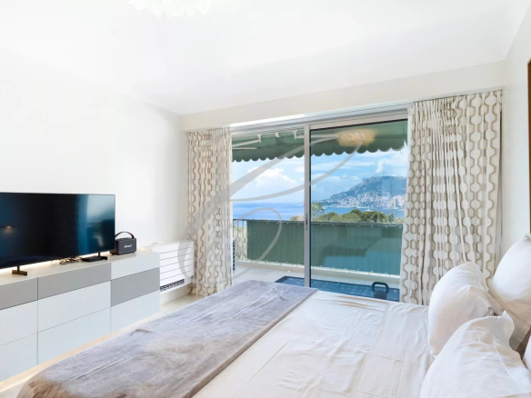 Chambre avec vue sur la mer et Monaco, lit et télévision, baie vitrée ouverte sur la terrasse.