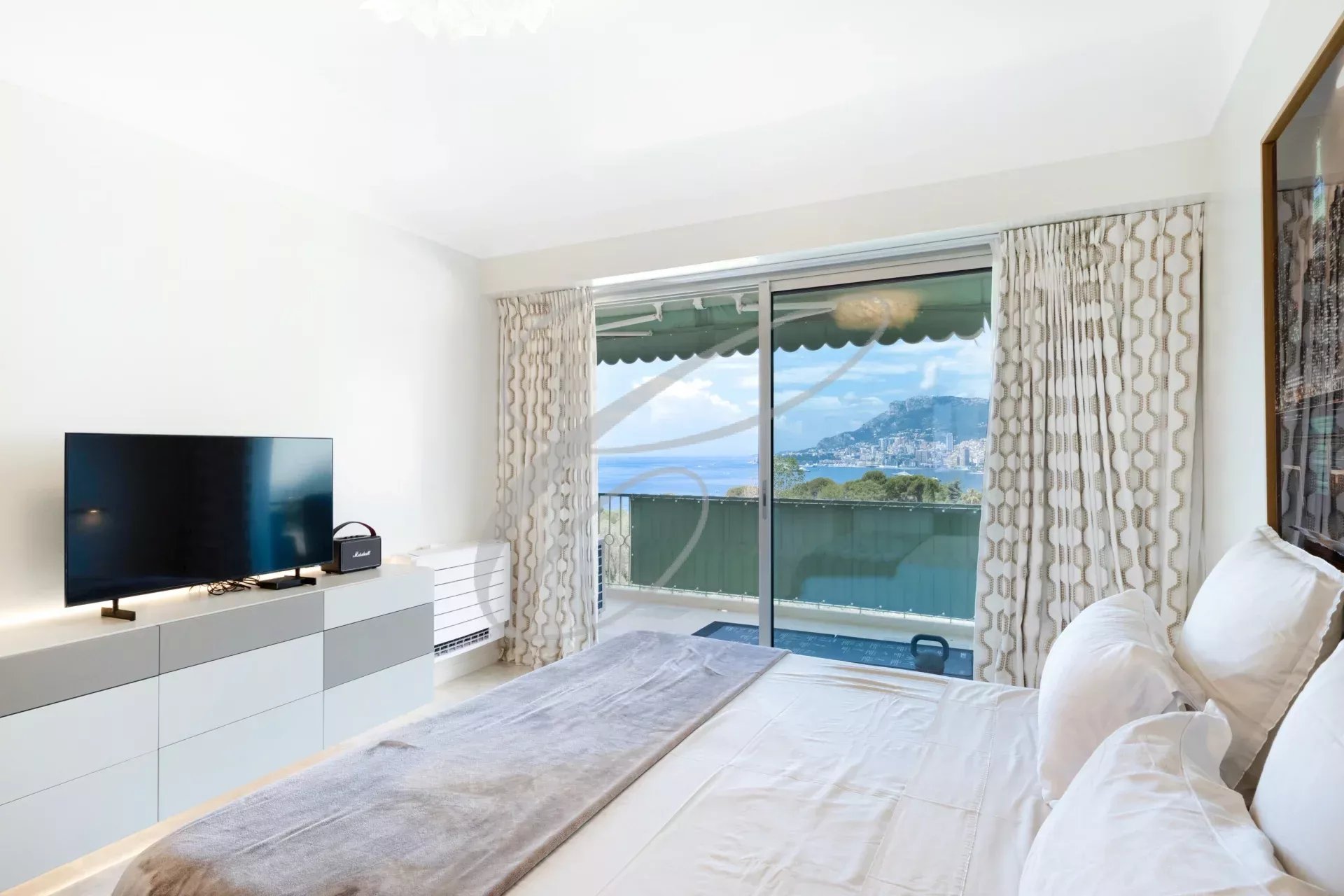 Chambre avec vue sur la mer et Monaco, lit et télévision, baie vitrée ouverte sur la terrasse.