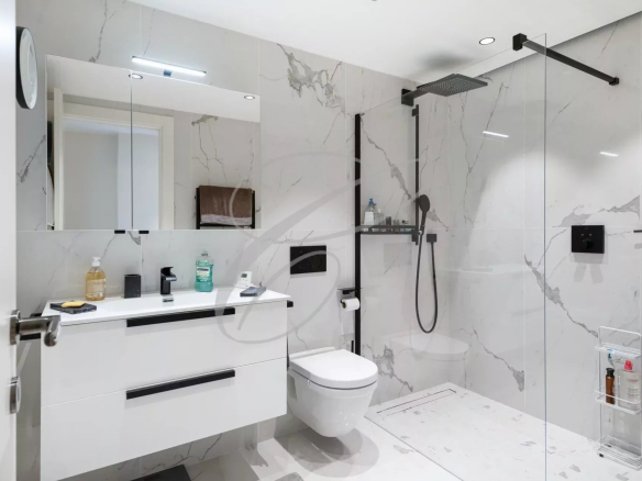 Salle de bains moderne avec douche, lavabo et toilettes, décorée de carreaux en marbre.