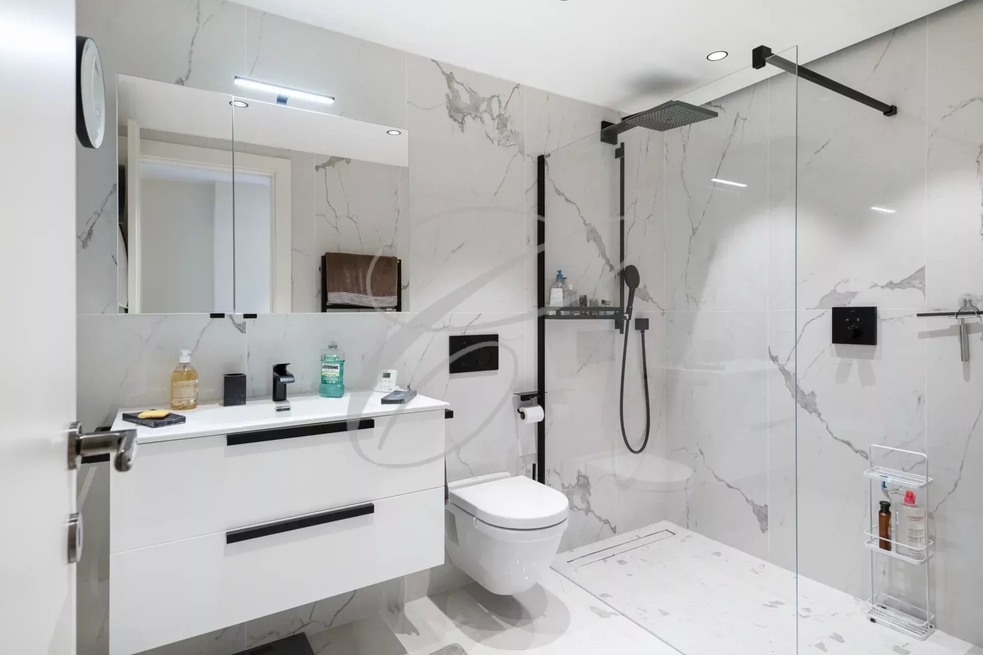 Salle de bains moderne avec douche, lavabo et toilettes, décorée de carreaux en marbre.
