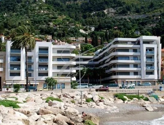 Immeuble moderne en bord de mer à Menton, avec piscine et espaces verts.