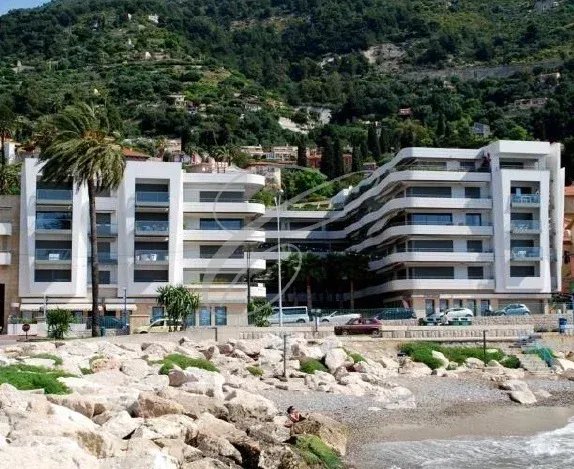 Immeuble moderne en bord de mer à Menton, avec piscine et espaces verts.